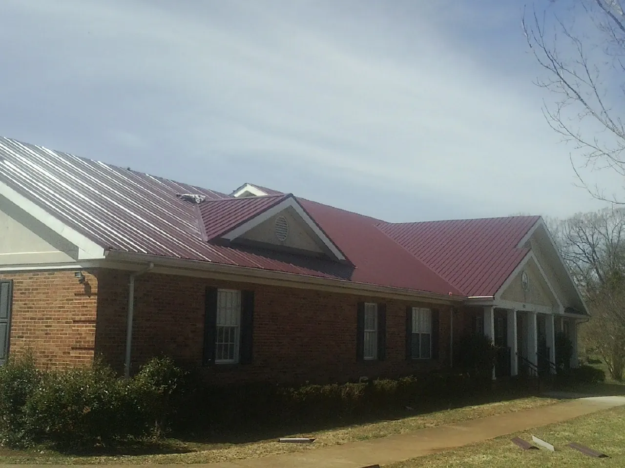 Red metal roof with gabled entries on a long brick building, from a Hail Damage Roof Repair job in Beallsville
