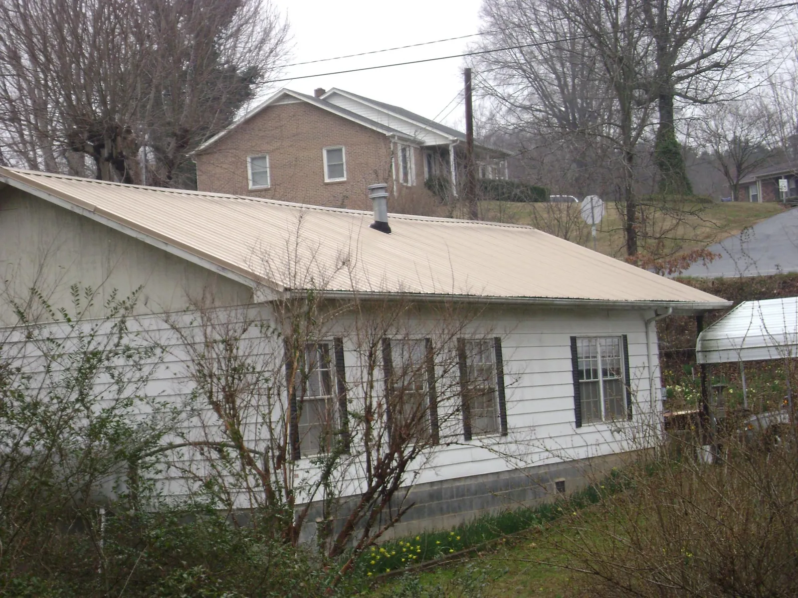 Tan metal roof on a white sided house set into a hillside — Commercial Roofing by Roofing Brothers in Beallsville